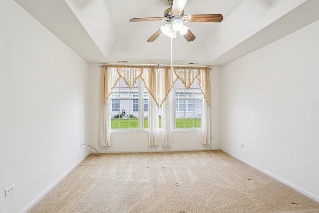 empty room with a ceiling fan, carpet floors, a raised ceiling, and baseboards