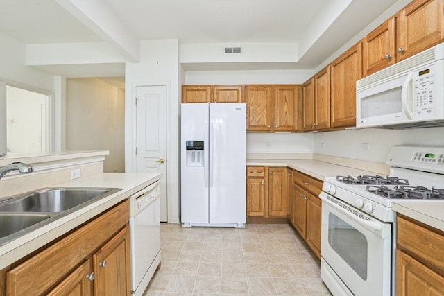 kitchen featuring white appliances, a sink, brown cabinetry, and light countertops