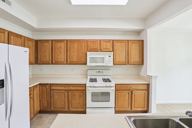kitchen with white appliances, brown cabinets, light countertops, and a sink