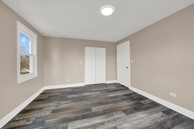 unfurnished bedroom featuring dark wood finished floors, baseboards, and a closet