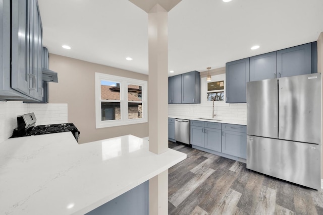 kitchen featuring stainless steel appliances, a sink, backsplash, wood finished floors, and recessed lighting