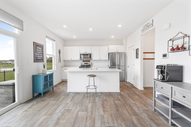 2461 Tahoe Ln, Pingree Grove, IL 60140 - kitchen with appliances with stainless steel finishes, light wood-type flooring, white cabinetry, a center island with sink, and light countertops