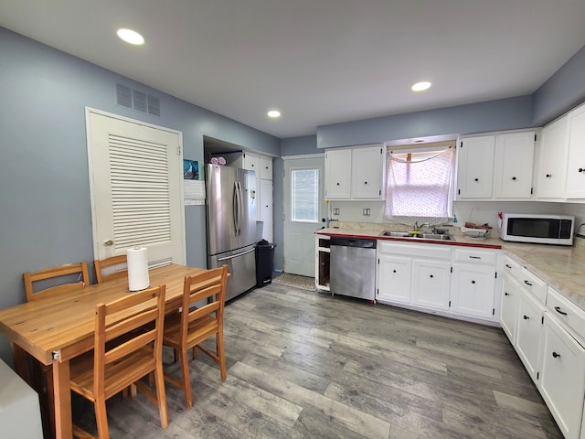 kitchen with stainless steel appliances, white cabinets, a sink, wood finished floors, and recessed lighting