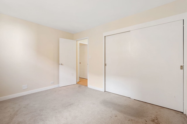unfurnished bedroom featuring light colored carpet, baseboards, and a closet