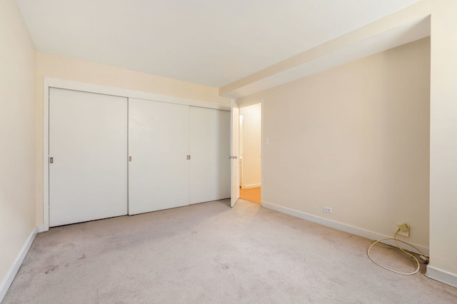 unfurnished bedroom featuring light colored carpet, a closet, and baseboards