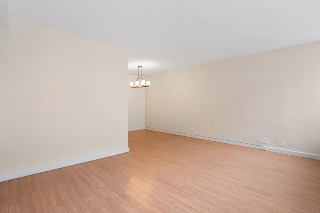 unfurnished room featuring a chandelier, light wood-style floors, and baseboards