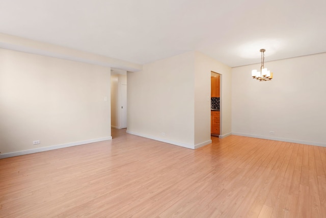 unfurnished room featuring a chandelier, light wood-style flooring, and baseboards