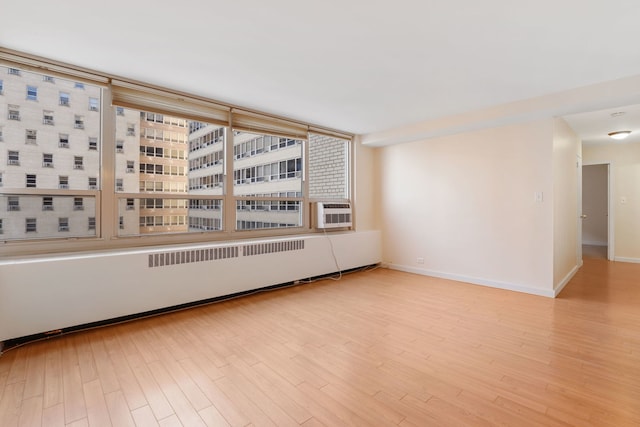 empty room featuring wood finished floors, baseboards, and radiator