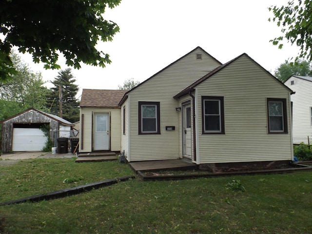 view of front of house featuring a detached garage, a front yard, an outdoor structure, and roof with shingles