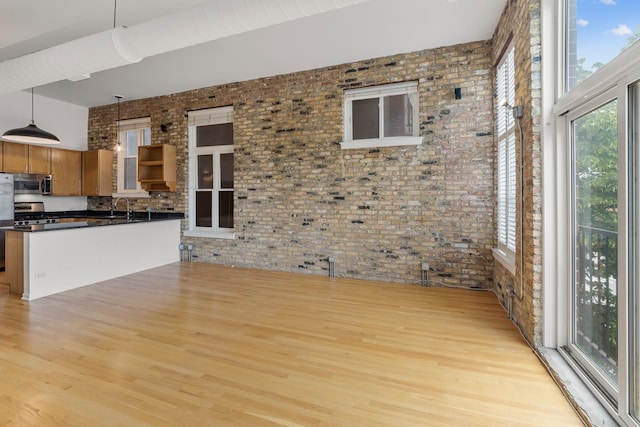 1012 W Diversey Pkwy Unit 2, Chicago, IL 60614 - kitchen with stainless steel appliances, dark countertops, brick wall, light wood-style flooring, and a towering ceiling