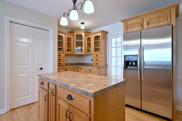 kitchen with stainless steel refrigerator with ice dispenser, glass insert cabinets, a kitchen island, and light wood-style flooring