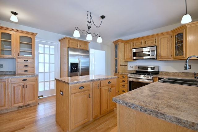 kitchen featuring appliances with stainless steel finishes, a sink, a kitchen island, light wood finished floors, and decorative light fixtures