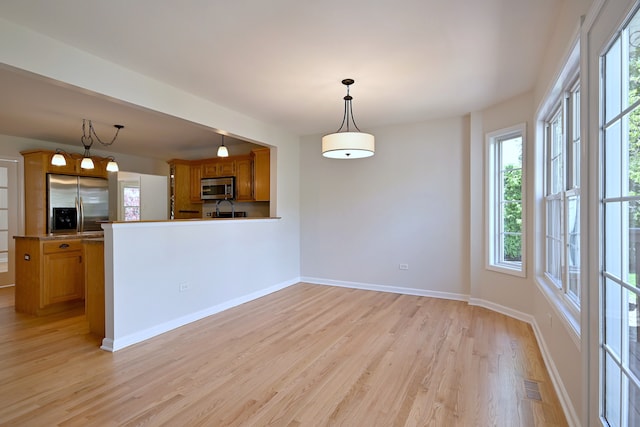 kitchen featuring stainless steel appliances, plenty of natural light, brown cabinetry, and light wood-style flooring
