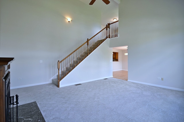 unfurnished living room featuring ceiling fan, carpet floors, stairway, baseboards, and a high ceiling