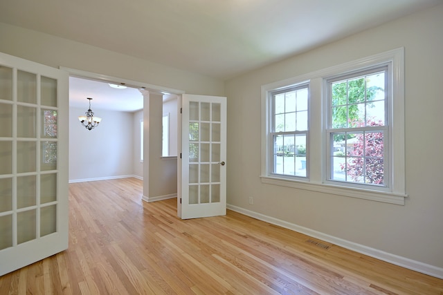 unfurnished room with a chandelier, light wood finished floors, baseboards, french doors, and ornate columns