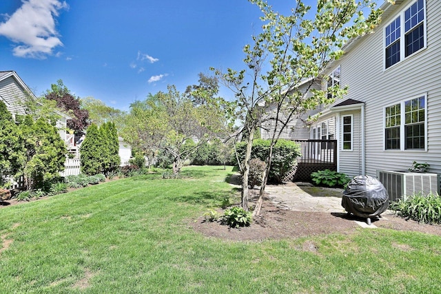 view of green lawn featuring a wooden deck and central AC