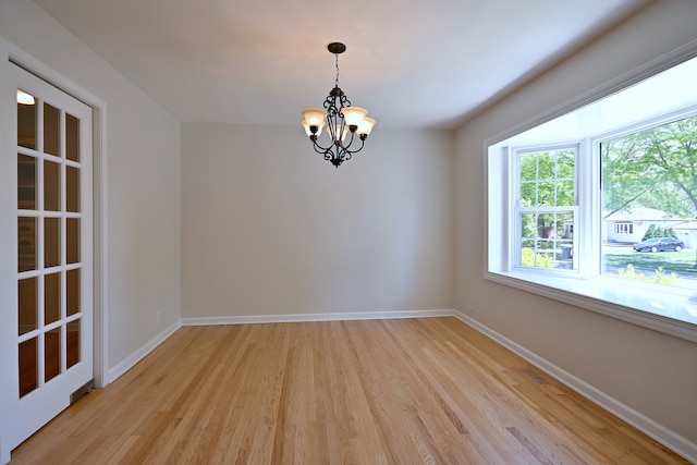 empty room with a chandelier, light wood finished floors, and baseboards