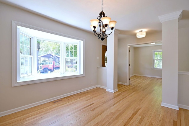 empty room featuring a chandelier, light wood-type flooring, and baseboards