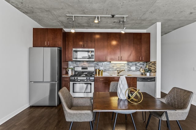 kitchen with stainless steel appliances, baseboards, dark wood-style floors, a sink, and track lighting