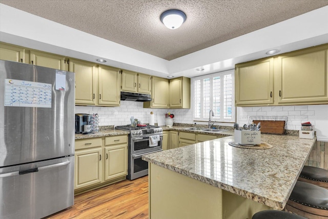 705 Northridge Dr, Mahomet, IL 61853 - kitchen featuring stainless steel appliances, under cabinet range hood, a textured ceiling, a peninsula, and a kitchen bar