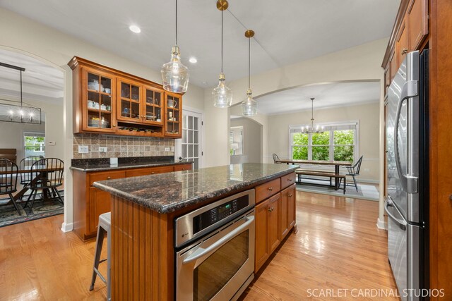 203 E Lincoln Ave, Wheaton, IL 60187 - kitchen featuring appliances with stainless steel finishes, brown cabinets, light wood-style flooring, decorative backsplash, and arched walkways
