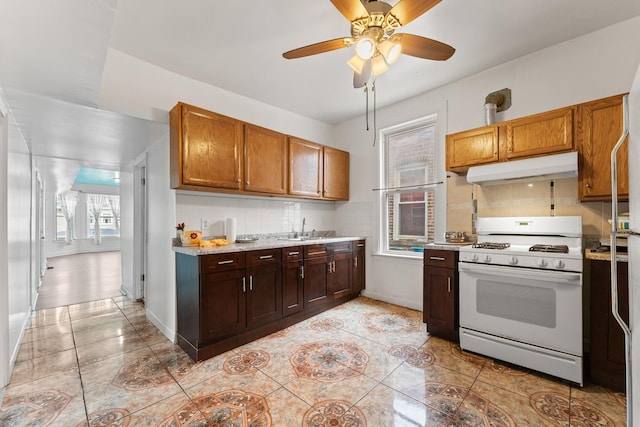 4947 W Huron St, Chicago, IL 60644 - kitchen featuring white gas stove, under cabinet range hood, a sink, and light tile patterned floors