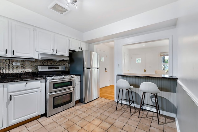 128 8th St, Downers Grove, IL 60515 - kitchen featuring appliances with stainless steel finishes, under cabinet range hood, white cabinets, backsplash, and light tile patterned flooring