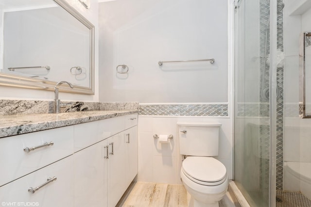 bathroom with toilet, tile walls, vanity, wainscoting, and a tile shower