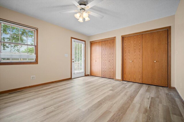8491 Surrey Cir, Bloomington, IL 61705 - unfurnished bedroom featuring two closets, light wood-type flooring, multiple windows, baseboards, and a textured ceiling