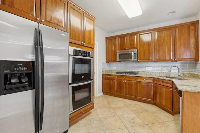 kitchen with appliances with stainless steel finishes, a sink, brown cabinets, and tasteful backsplash