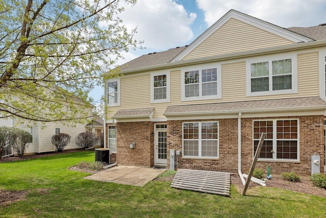 back of property featuring a patio area, brick siding, a yard, and a shingled roof
