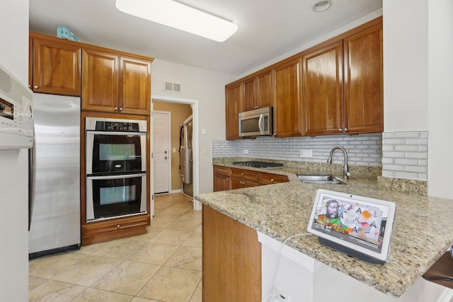 kitchen with a sink, appliances with stainless steel finishes, a peninsula, light stone countertops, and decorative backsplash