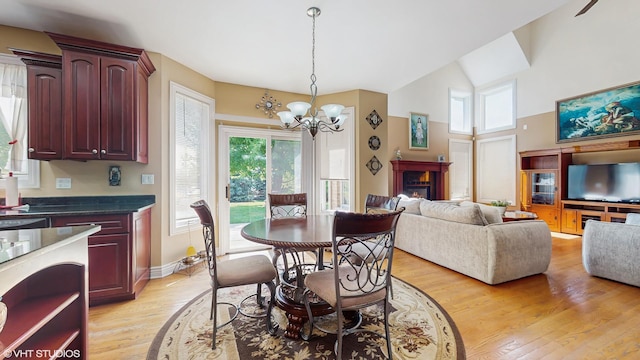 17040 Cheyenne Ct, Lockport, IL 60441 - dining space with a chandelier, light wood-style flooring, a warm lit fireplace, a towering ceiling, and baseboards