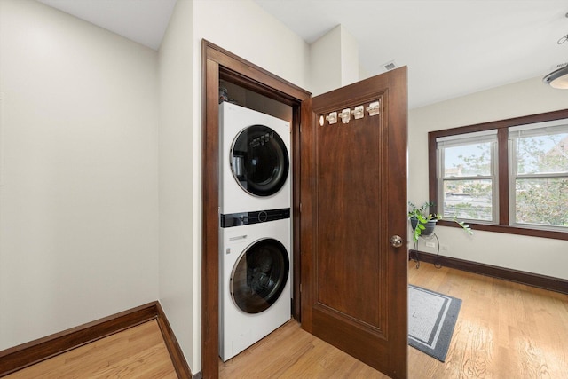 laundry room featuring stacked washer / drying machine, light wood-style flooring, and baseboards