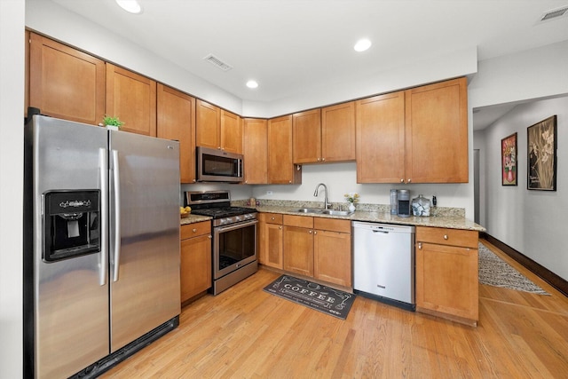 kitchen with appliances with stainless steel finishes, a sink, light stone countertops, light wood finished floors, and recessed lighting