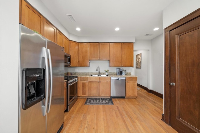 kitchen with stainless steel appliances, a sink, brown cabinets, light wood-type flooring, and baseboards