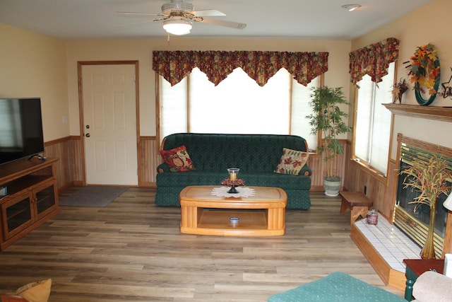 living room featuring plenty of natural light, wood finished floors, a wainscoted wall, ceiling fan, and a tiled fireplace