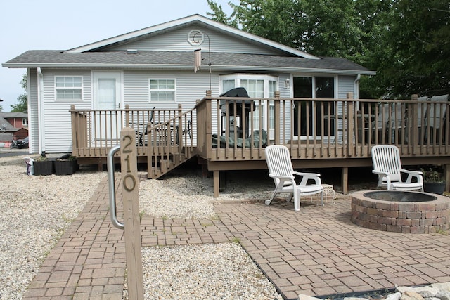 back of property with a fire pit, a patio area, a deck, and roof with shingles