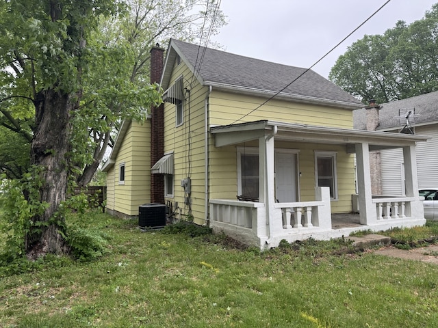 view of home's exterior featuring a chimney, a porch, a yard, and cooling unit