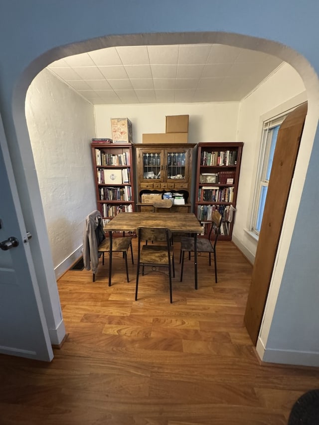 dining space with arched walkways, baseboards, and wood finished floors