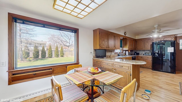 7421 N Crossway Rd, Fox Point, WI 53217 - kitchen with black fridge with ice dispenser, a peninsula, tasteful backsplash, light wood-style flooring, and a sink