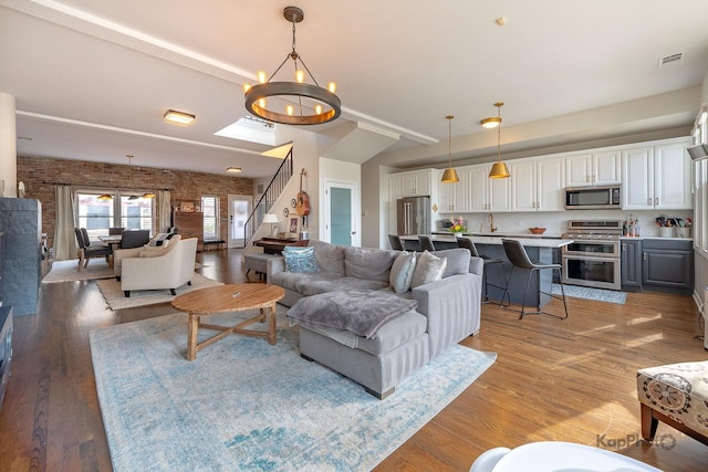 2044 W Roscoe St Unit 2S, Chicago, IL 60618 - living room with stairs, light wood-style flooring, a chandelier, and brick wall