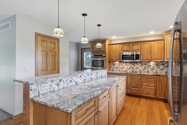 717 S Kennedy St, Shannon, IL 61078 - kitchen featuring appliances with stainless steel finishes, light wood-style flooring, a center island, backsplash, and light stone counters