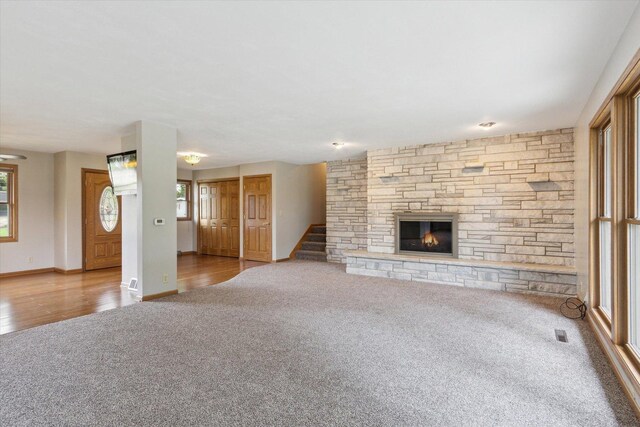 717 S Kennedy St, Shannon, IL 61078 - unfurnished living room featuring carpet flooring, a stone fireplace, stairs, baseboards, and wood finished floors
