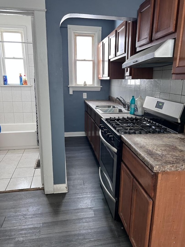 301 W 104th St, Chicago, IL 60628 - kitchen with stainless steel gas stove, under cabinet range hood, baseboards, a sink, and backsplash