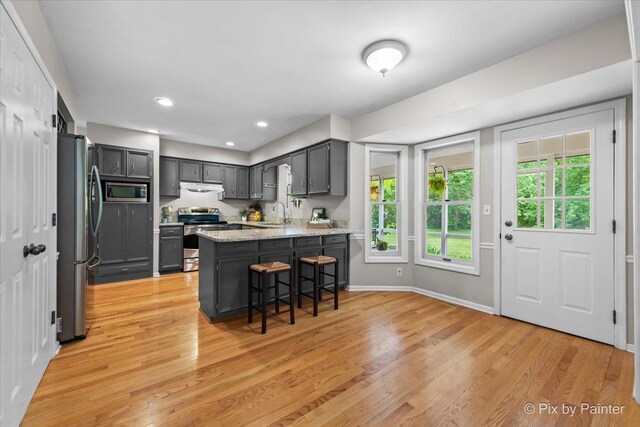 39W889 Deer Run Dr, Saint Charles, IL 60175 - kitchen with appliances with stainless steel finishes, a peninsula, light wood-style floors, light stone countertops, and a kitchen bar