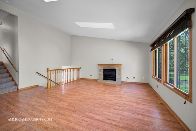 211 Lorien Ct, East Dundee, IL 60118 - unfurnished living room with a skylight, lofted ceiling, light wood-type flooring, a brick fireplace, and baseboards
