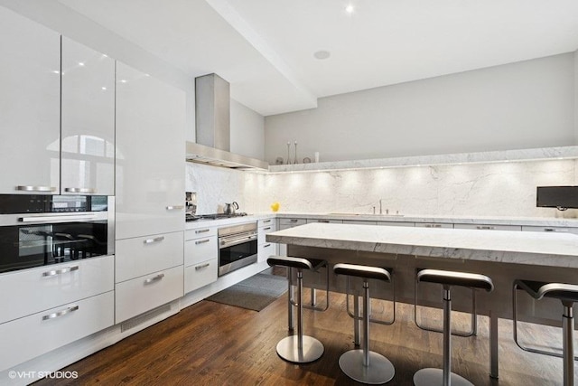 1733 S Prairie Ave, Chicago, IL 60616 - kitchen featuring stainless steel oven, wall chimney range hood, modern cabinets, and a kitchen bar