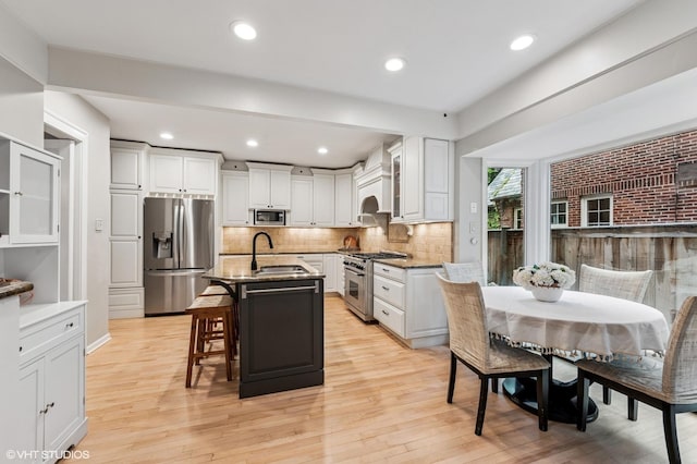 350 Elder Ln, Winnetka, IL 60093 - kitchen with appliances with stainless steel finishes, a sink, a kitchen breakfast bar, light wood-style flooring, and stone countertops