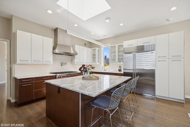 2122 N Hudson Ave, Chicago, IL 60614 - kitchen featuring appliances with stainless steel finishes, wall chimney range hood, dark wood finished floors, a kitchen breakfast bar, and glass insert cabinets
